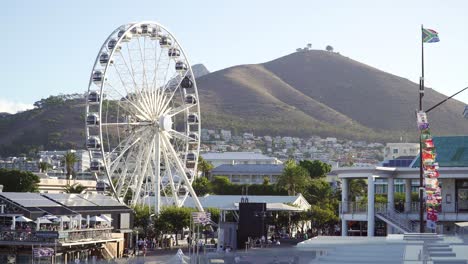 ferris wheel on touristic waterfront in cape town with signal hill in background