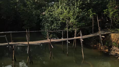 slow close-up aerial shot of a wooden bridge over a river on the rainforest island of koh chang, thailand