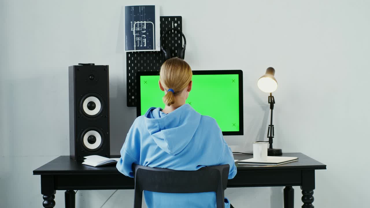 녹색 모니터 앞에 앉아 있는 카메라를 보고 미소 짓는 젊은 여성