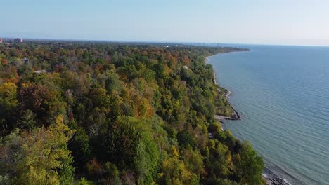 Flying-over-Lake-Ontario-as-waves-crash-along-colorful-treed-Scarborough-Bluffs-escarpment