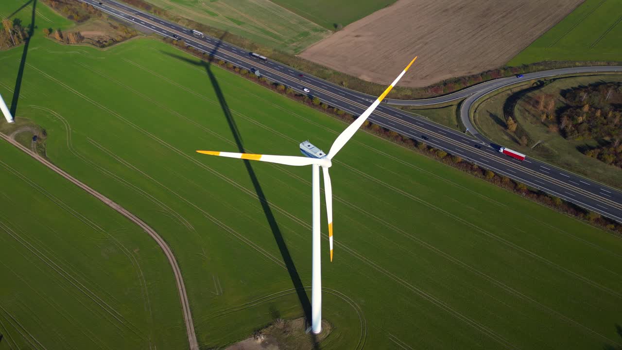 Wind turbine standing in green field next to highway autobahn in autumn Germany, generating renewable energy. Best aerial view flight drone shot from above
