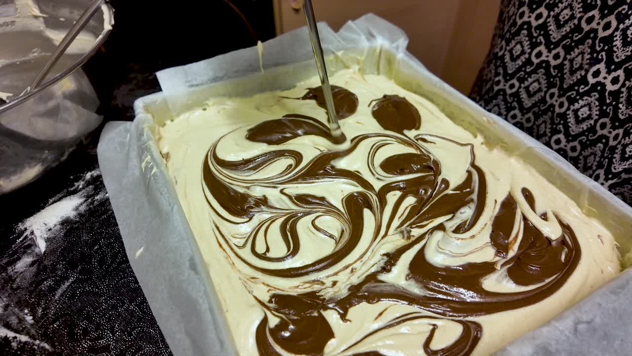 Swirling melted chocolate into light cake batter for a marble effect in a baking pan