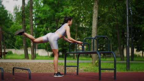 a young caucasian woman lifts her legs back while standing in a park on a sports field in the summer. a woman does sports in the summer alone in the park.