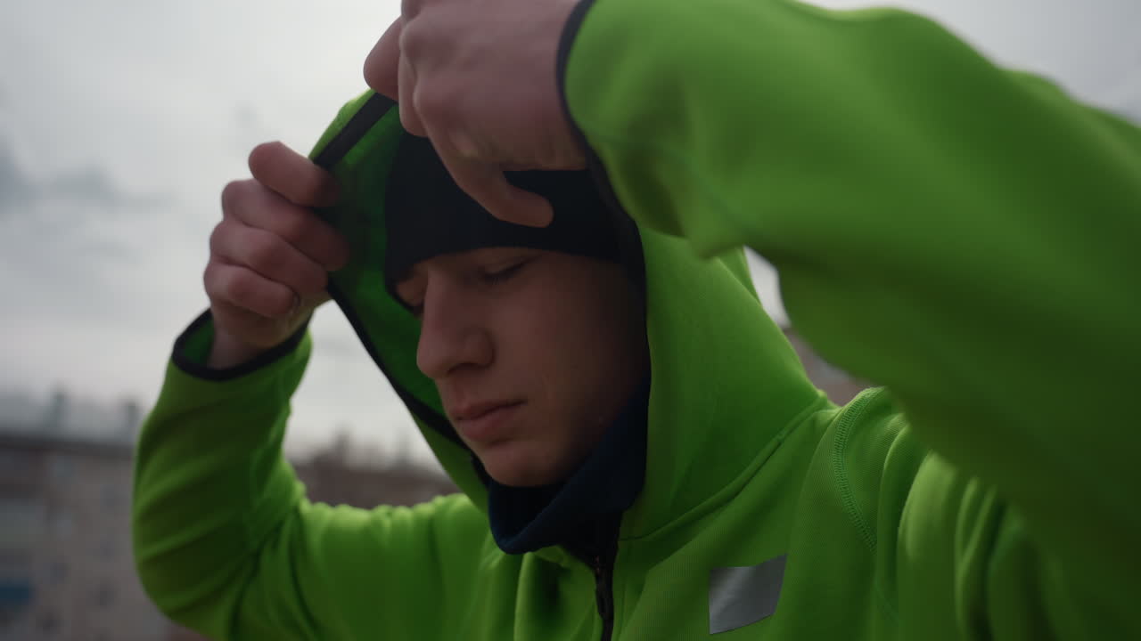 추운 날씨에 옷을 정리하는 남자, 추운 야외 운동 중에 모자를 고정하는 사람, 추운 야외 환경에서 후드티와 마스크를 조정하는 데 집중하는 남성