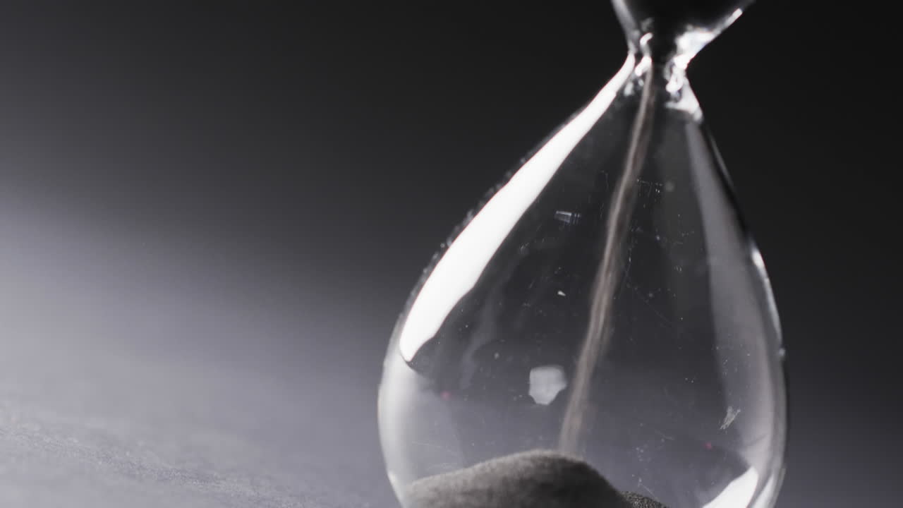 Video of hourglass with sand pouring, copy space on black background