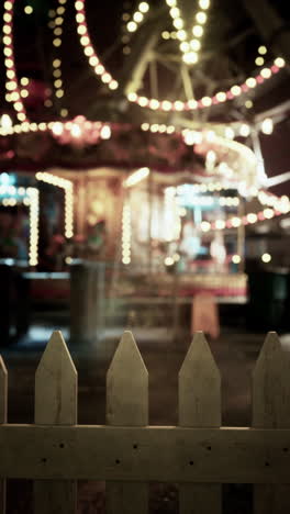 a blurred image of a carousel through a white fence at night