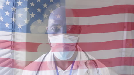 animation of american flag and spots over african american male doctor in face mask