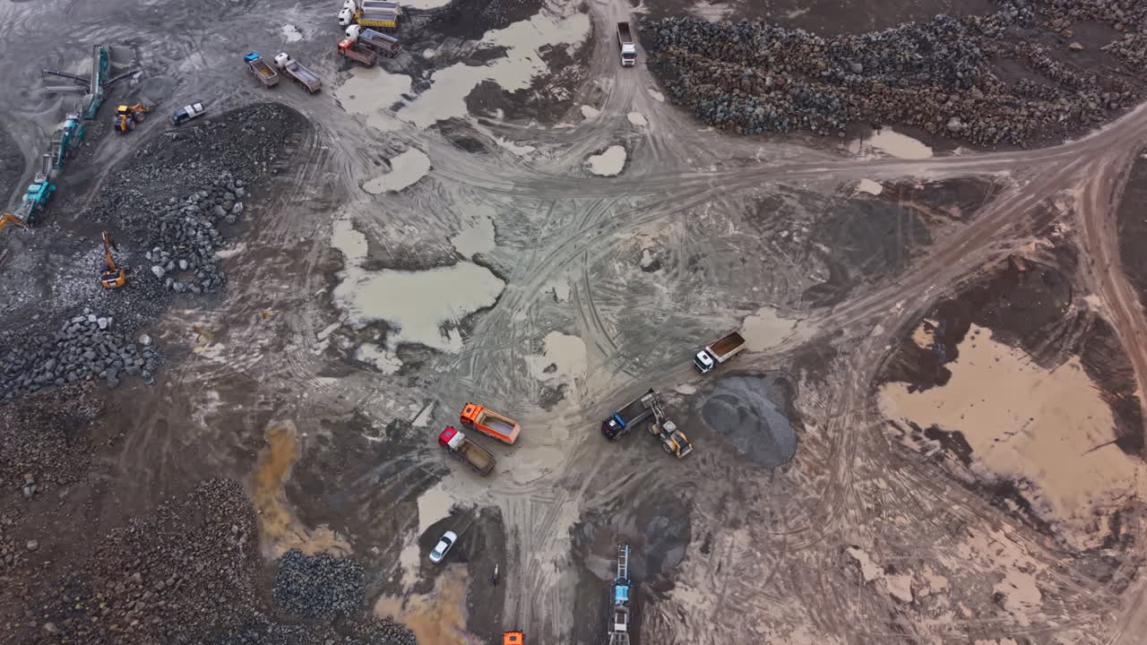 Heavy machinery works in granite quarry with trucks and equipment at daytime in busy operation