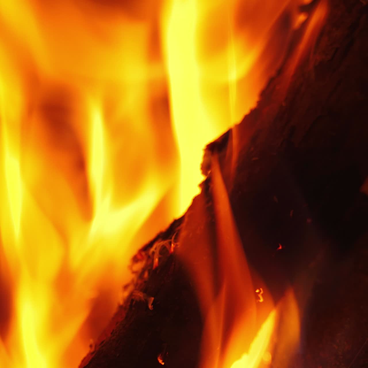 Vivid flame on wooden logs. Orange and yellow fire burning in fireplace. Bright motion of fire tongues. Macro shot.