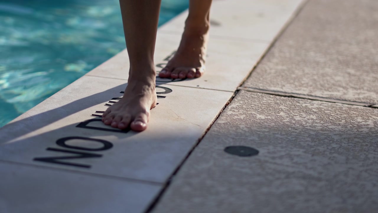 woman walking barefoot during the day across the ledge by a pool