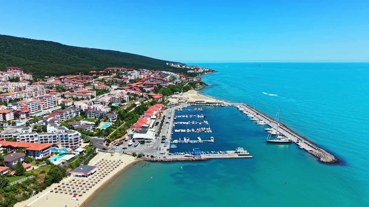 Berrak Mavi Gökyüzü ve Sakin Denize Sahip Güneşli Bir Günde, Bir Tatil Kasabasında Marina ve Plaj Alanını Gösteren Kıyı Manzarası