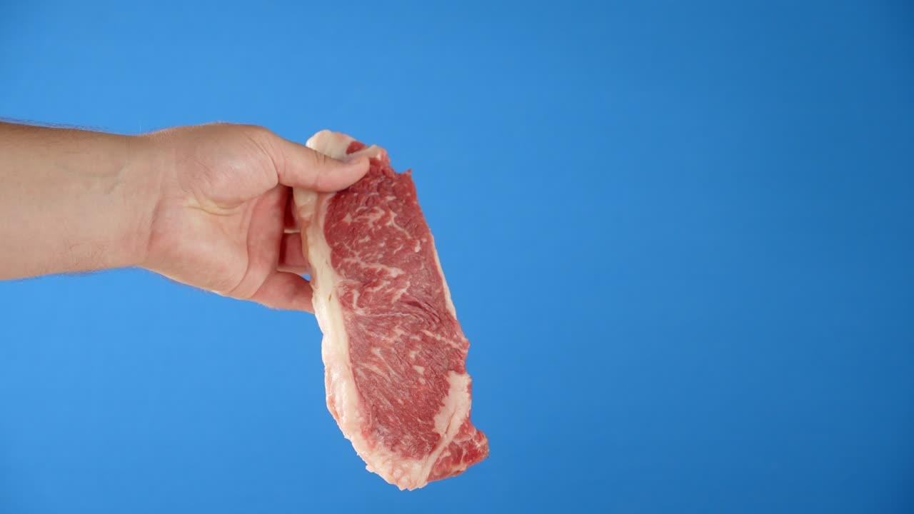 한 남자의 손은 스테이크 원시 고기 스트리플로인을 들고 있습니다.