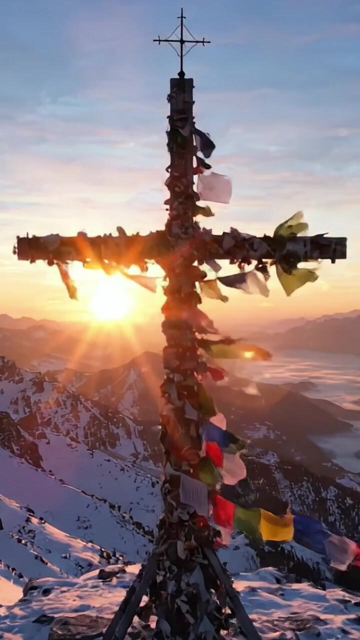 Majestic Sunrise Over a Mountain Cross with Colorful Prayer Flags, Capturing the Serene Beauty of Nature as the Dawn Breaks