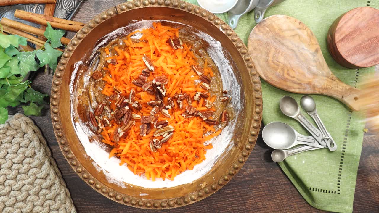 Baking a carrot cake loaf with cream cheese icing and topped with roasted salted pecans. Making a Autumn dessert with carrots, flour, sugar, nuts and frosting. Mixing in the pecans to the batter.