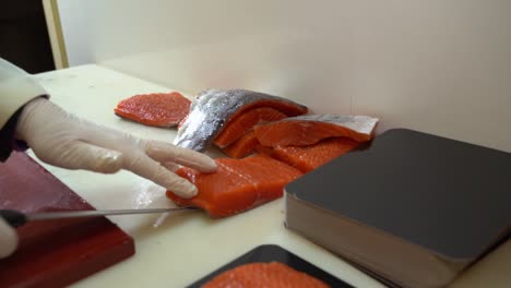 salmon industry worker in white coat moving salmon filet from chopboard to cutting table - slow motion