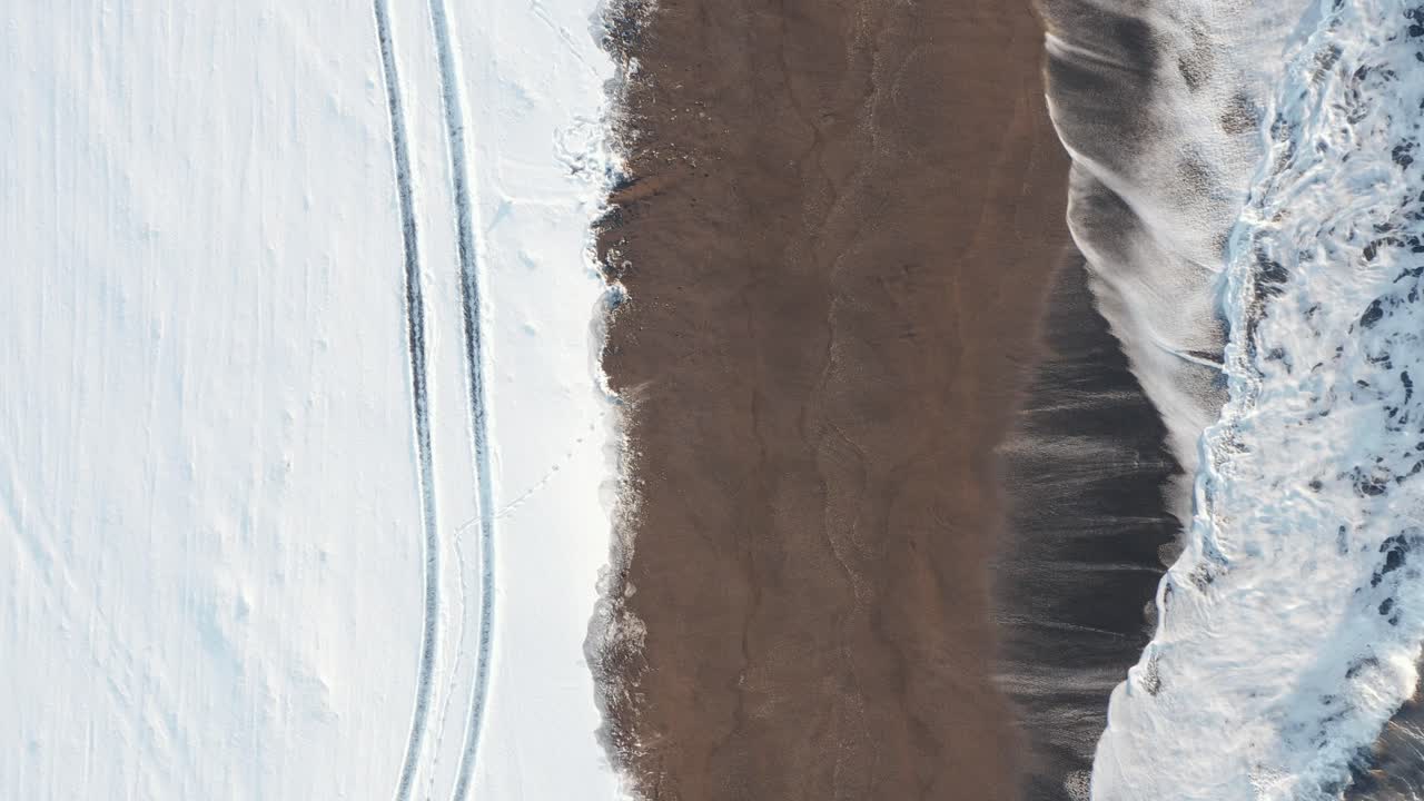 Le onde si infrangono sulla riva della spiaggia di Sandvík coperta di neve in Islanda, vista dall'alto.