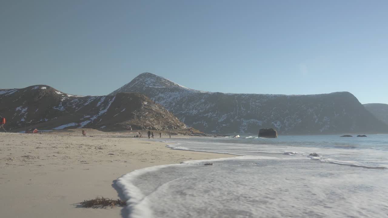 волны мягко набегают на пляж с суровыми горами лофотен на заднем плане