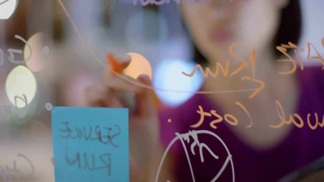 Asian casual businesswoman brainstorming, making notes on glass wall at night in office