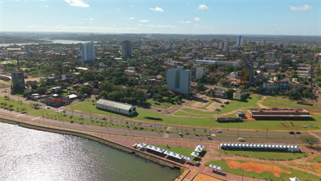 aerial shot of encarnación city waterfront with green park and local riverside buildings, itapúa, paraguay