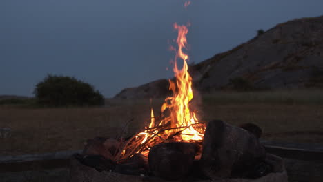 a cosy bonfire burning next to a field and a hill in slow-motion