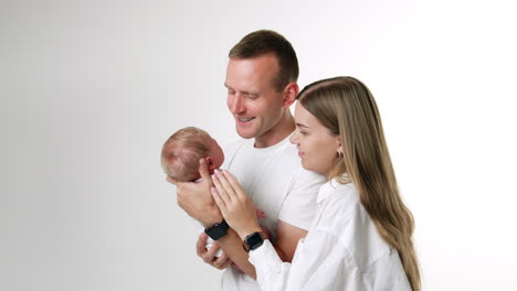 lovely caucasian family of three. parents in white t-shirts hold their beloved newborn son. white backdrop.