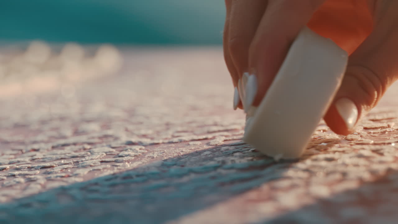 Female hand applies wax to pink surf board in extreme slow motion