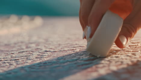 female hand applies wax to pink surf board in extreme slow motion