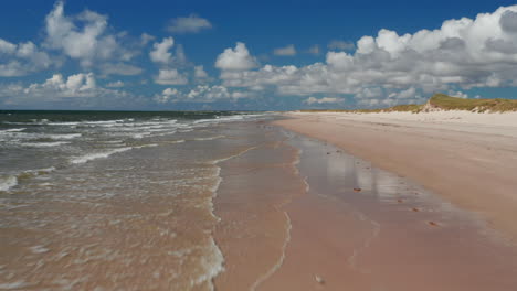 Low-flight-above-coastline.-Waves-washing-sandy-beach-on-sunny-day.-Summer-vacation-location.-Denmark
