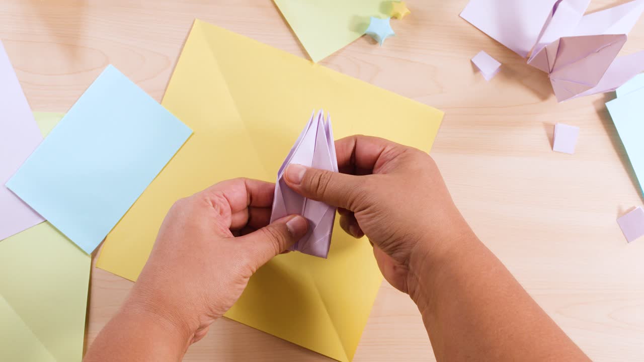 Primo piano dall'alto di mani che piegano con cura un foglio di carta viola a forma di uccello origami