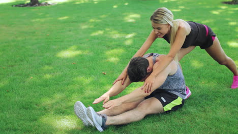 Mujer-Entrenadora-Deportiva-Ayuda-A-Un-Hombre-Fitness-Estirando-Las-Piernas-En-El-Parque-De-Verano