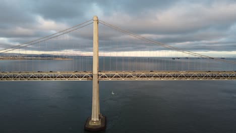 4k 30fps aerial drone close up flying footage of san francisco oakland bay bridge double suspension - cars travel along the highway, stormy cumulus clouds, calm bay water, sunset reflecting off waves