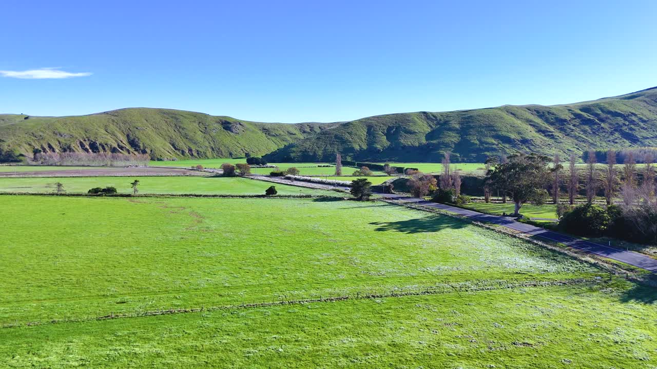 Aerial footage captures lush green fields and rolling hills under clear blue skies in Akaroa, New Zealand