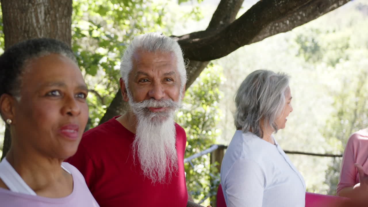 Amigos idosos diversos e felizes (homens e mulheres) segurando tapetes de yoga e conversando na natureza ensolarada, em câmera lenta