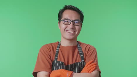 primer plano de un ama de casa asiático con un delantal sonriendo cálidamente y cruzando los brazos mientras está de pie en el estudio de pantalla verde