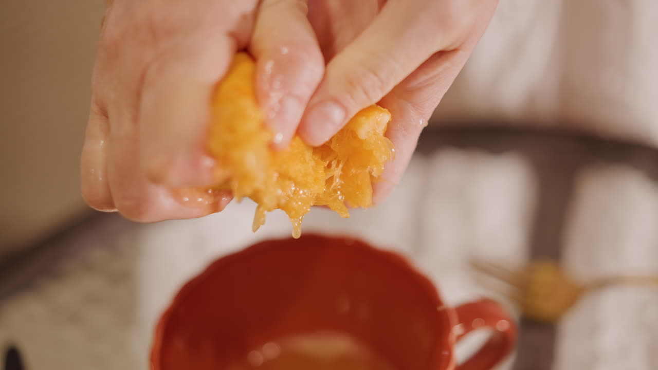 Manos vertiendo pulpa de fruta sobre una taza. Primer plano de pulpa fibrosa y semillas liberando jugo en una taza de cerámica, movimiento íntimo táctil de presión y liberación, preparación manual desordenada para conservas o jarabe, acogedor.