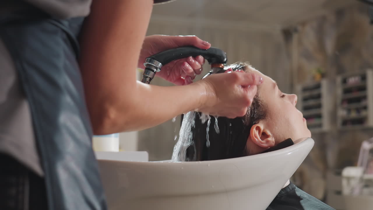 Hårvaskscene, stylist påfører vand i håret kraftigt, professionel vask med håndholdt spray ved salonvask, moderne salontekniker udfører hårskylning med kontrolleret vandstrøm