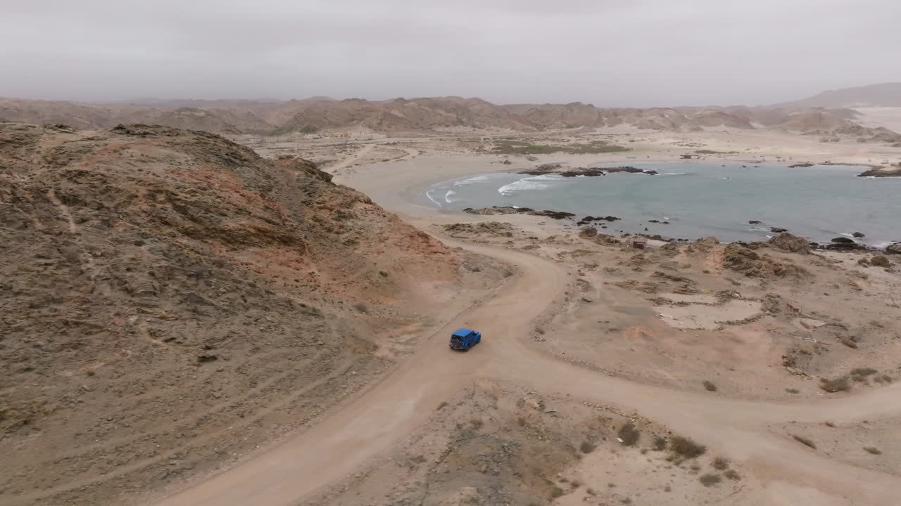 Winding coastal road through rugged terrain with a blue car on a scenic drive