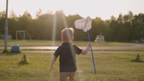 funny little boy runs holding hoop net along playground