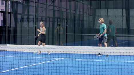 Young adults playing padel tennis on blue indoor court, focusing on ball