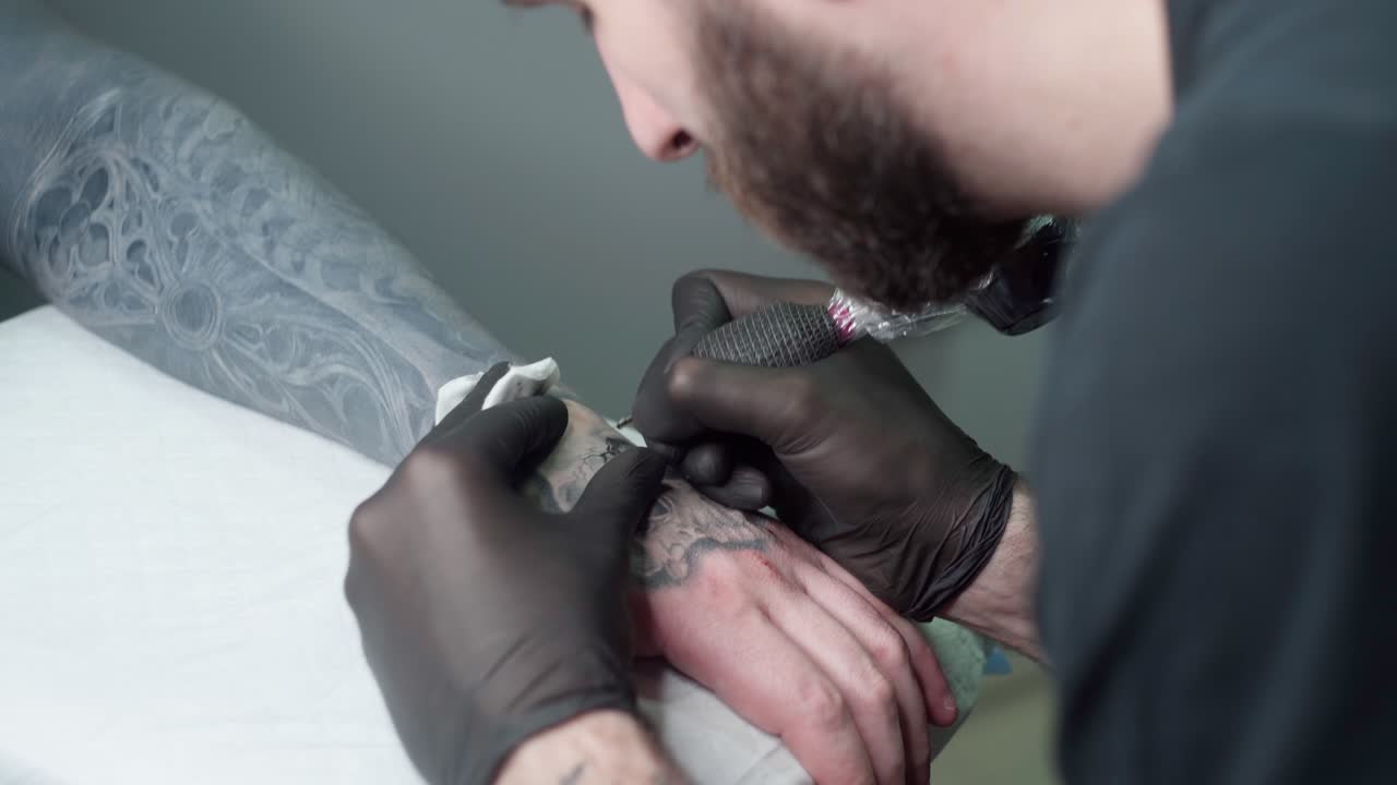Tatuatore che realizza un tatuaggio con la macchinetta su un braccio in un salone