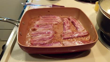 uncured bacon cooking in a square pan on an electric stove