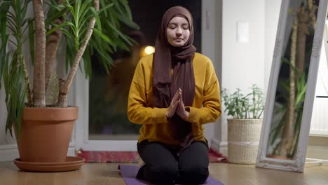 religious muslim woman praying sitting at home in the evening. front view portrait of concentrated confident young lady in hijab talking thinking indoors. religion and hope concept.