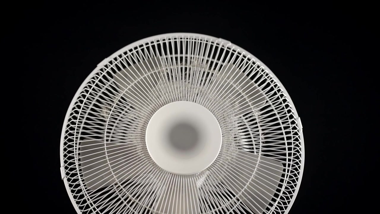 Hvid piedestalventilator fylder billedet i nærbillede mod en sort baggrund