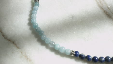 dolly macro shot of blue celestite beads from tibetan prayer mala placed on white marble shot in uhd