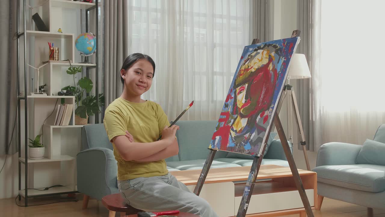 Asian Artist Girl Holding Paintbrush Crossing His Arm And Smiling After Finish Painting A Girl On The Canvas