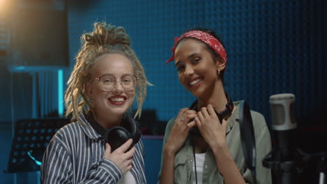 portrait of the two beautiful young female singers laughing ad having fun while recording song together in the sound studio