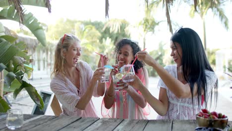 happy diverse female friends drinking cocktails at beach bar and talking