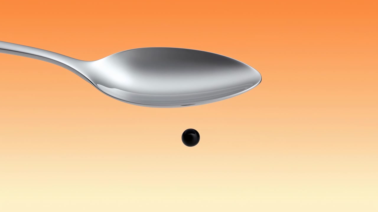 Close-up of a silver spoon with a glossy black droplet suspended beneath it against a warm orange and cream gradient background, lit with soft studio reflections in a minimal composition