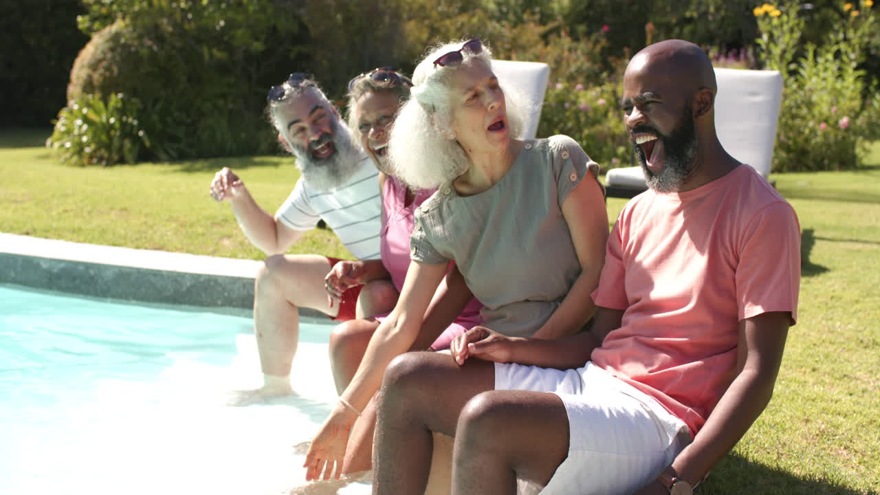 Sitting by pool, senior friends laughing and enjoying sunny day together