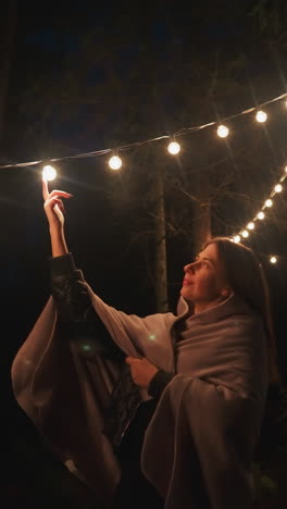 mujer pone el dedo en la lámpara en el campamento del bosque. mujer joven descubre la serenidad en la quietud y el aislamiento de retiro de glamping inmersión en la fusión de reposo